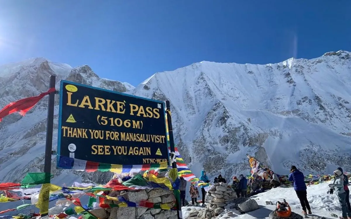 Larkya La Pass sign at 5,106m with prayer flags and snow-capped Himalayan peaks