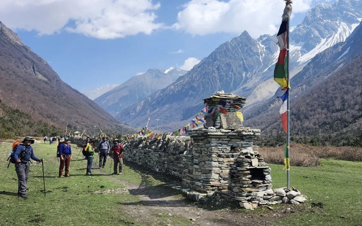 Trekkers at stone chorten with prayer flags in Manaslu valley surrounded by snow-capped mountains