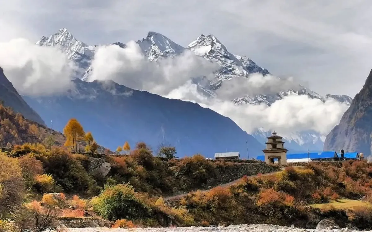 Traditional Buddhist monastery with autumn foliage and cloudy Himalayan peaks in background
