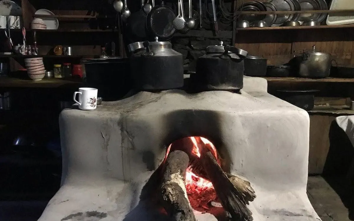 Traditional clay wood-burning stove with glowing fire in teahouse kitchen.