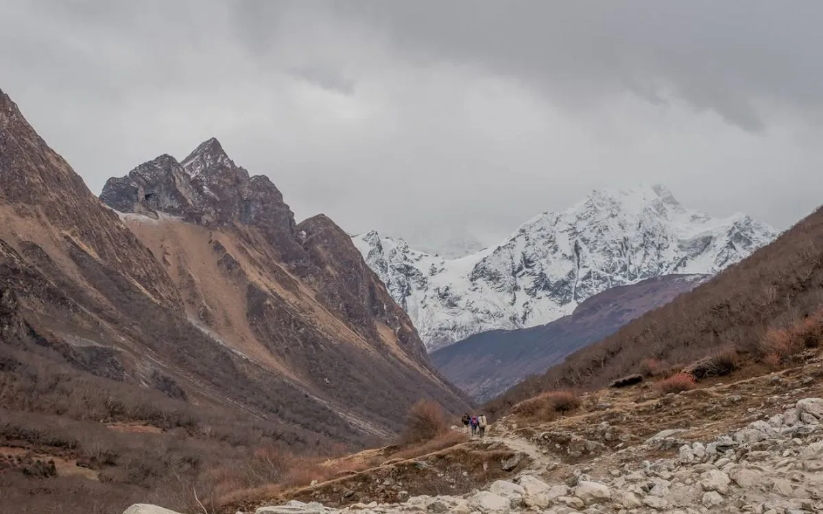 Trekkers walking mountain trail toward snowy peaks