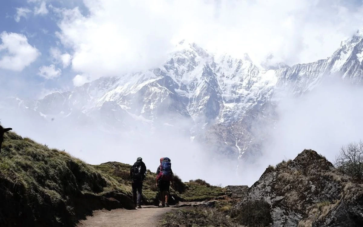 Two trekkers with backpacks on trail toward misty Himalayan peaks