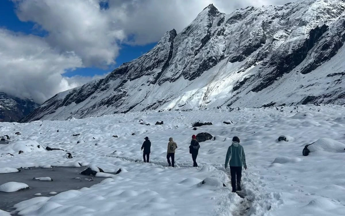 Four trekkers walking across snowy terrain with dramatic snow-covered peaks behind them