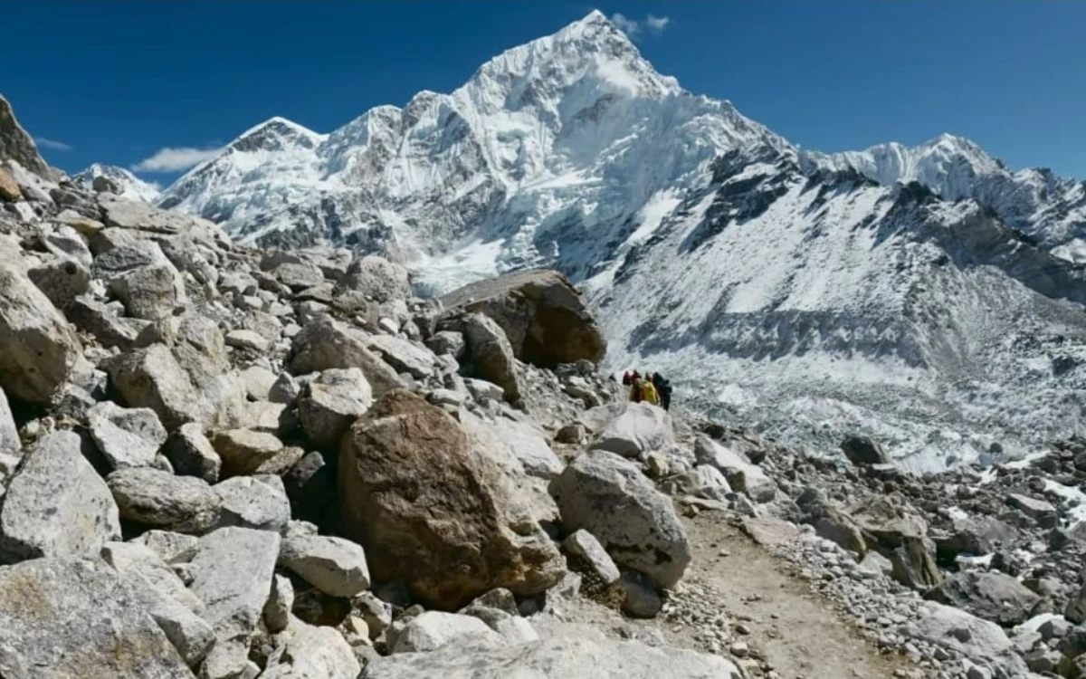 Hikers approaching rocky trail with glaciated mountain and ice formations visible
