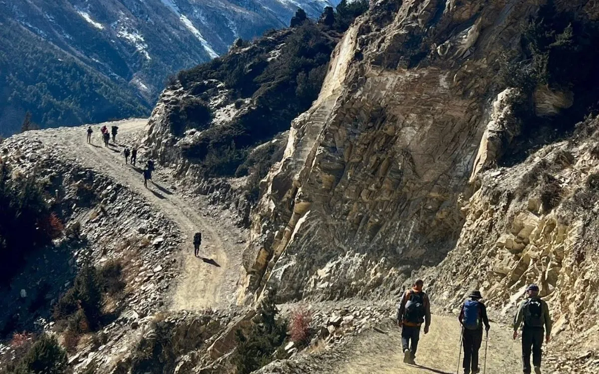 Trekkers hiking narrow mountain trail carved into rocky cliff face on Annapurna Circuit trek Nepal