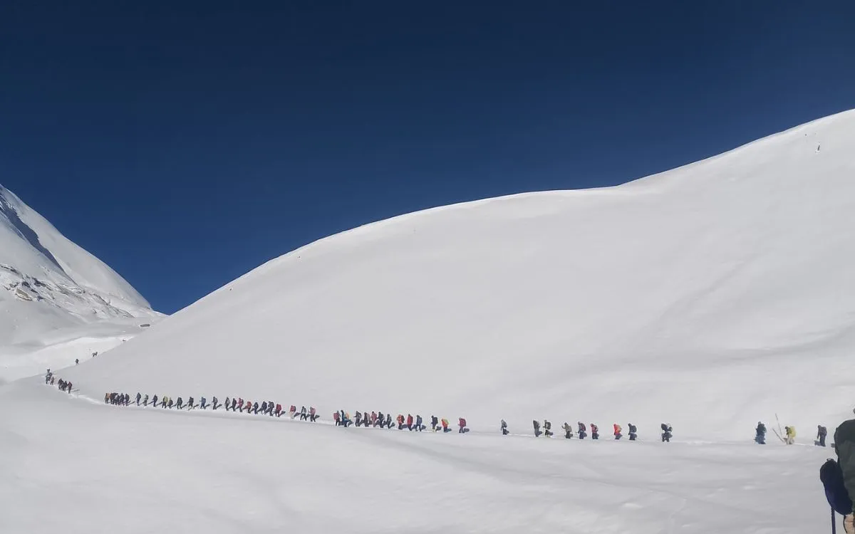 Long line of trekkers ascending snowy mountain pass on Annapurna Circuit trek in Nepal Himalayas