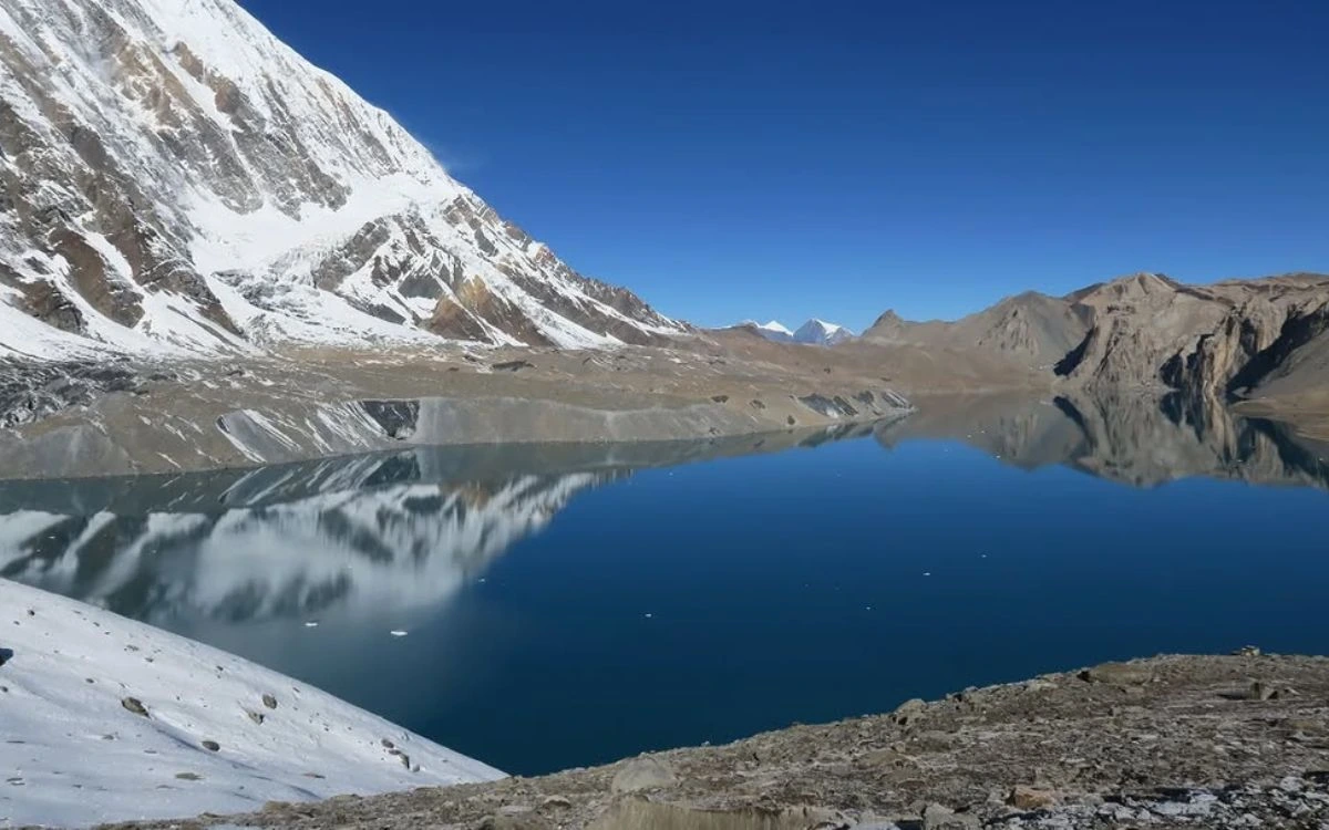 Tilicho Lake reflecting snow-covered peaks under a clear blue sky on the Annapurna Circuit