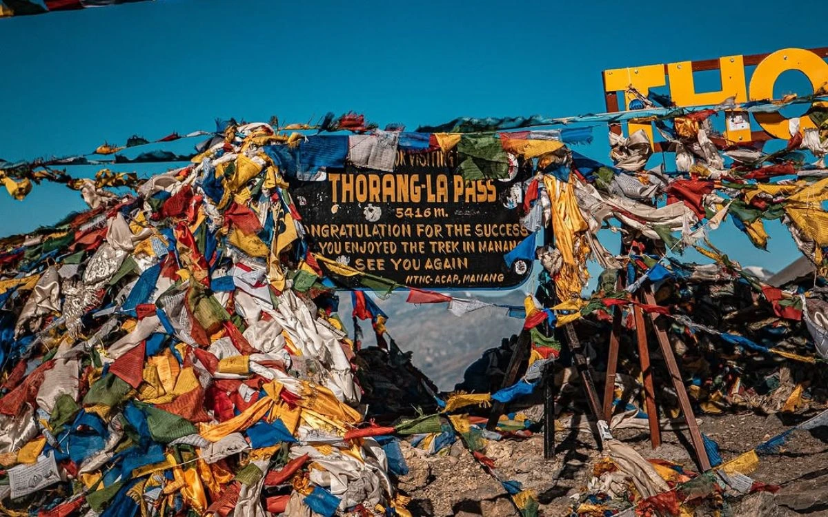 olorful prayer flags surrounding the Thorang La Pass summit sign at 5,416m on the Annapurna Circuit