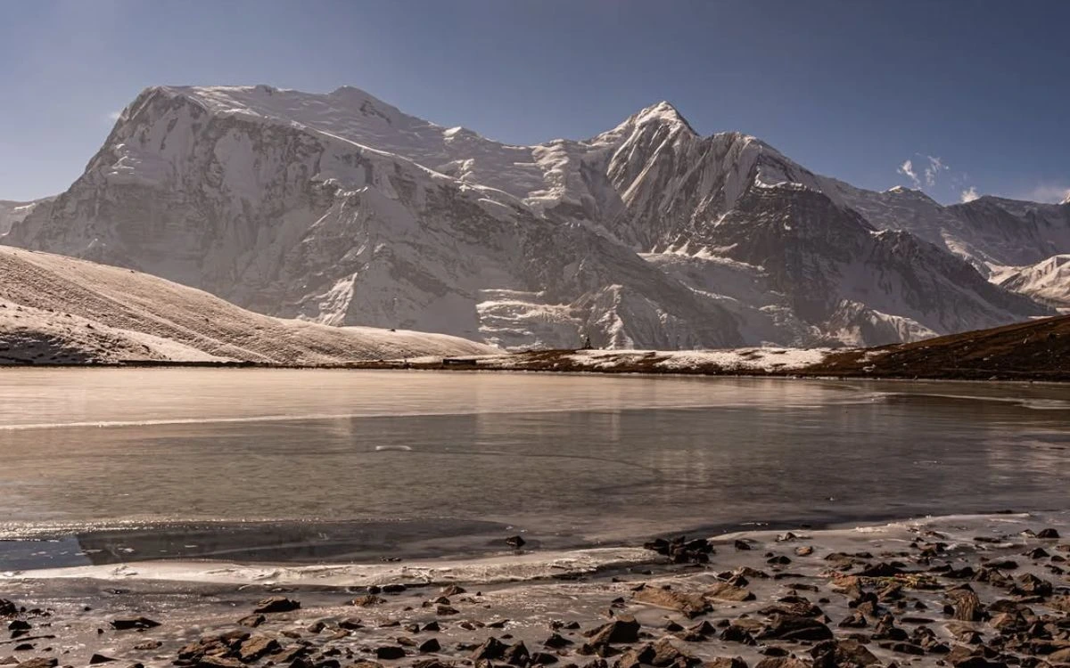 Frozen alpine lake reflecting mountain massif in high altitude landscape