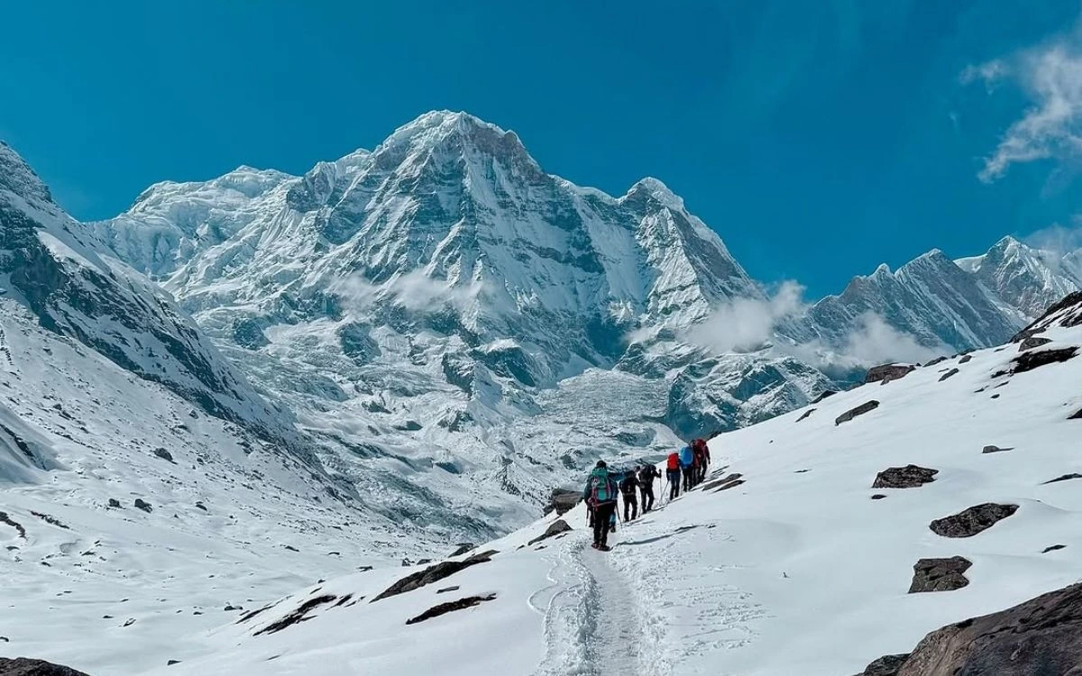 Trekkers hiking toward snow-covered Annapurna peak-I under clear blue sky