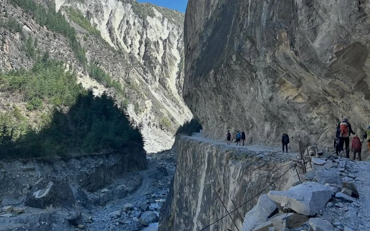 A group of trekkers navigating a narrow ledge trail high above a rocky gorge on the Annapurna Circuit