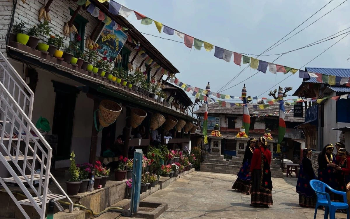 Prayer flags and women in traditional dress in a village on the ABC Trek