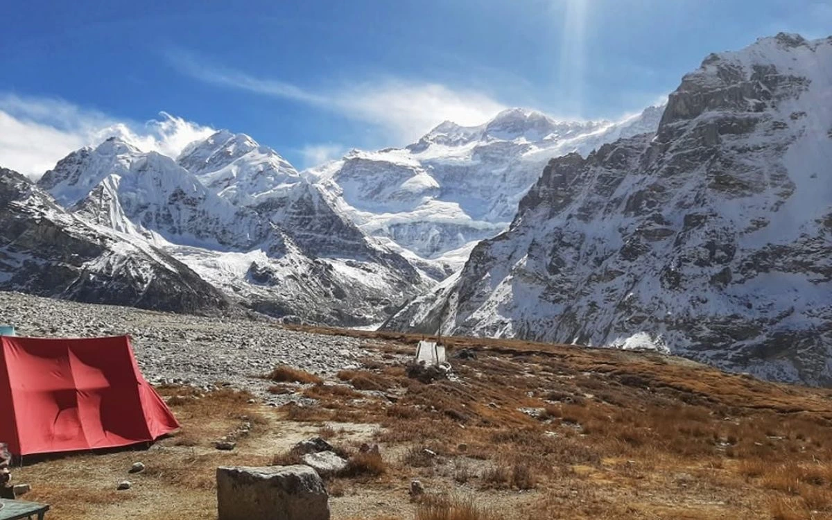Red tent in a snowy, rocky valley with clear sky and some grass