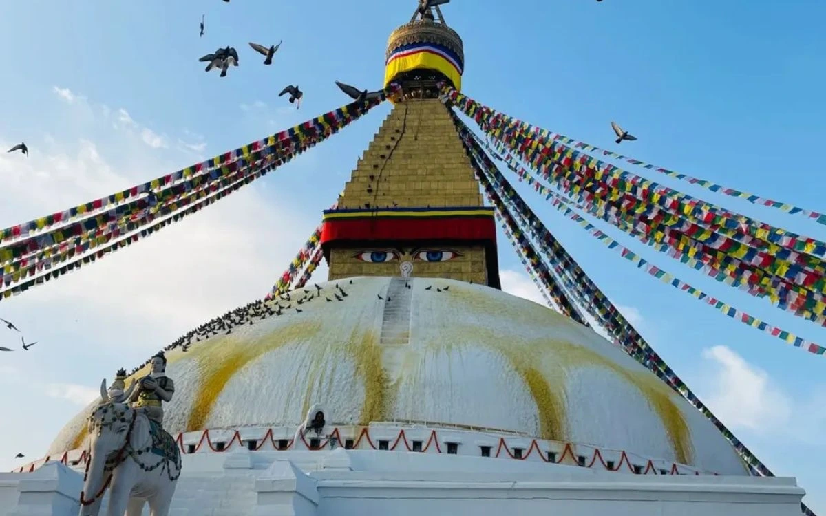 "Boudhanath Stupa Buddha eyes and prayer flags with pigeons flying around the golden spire