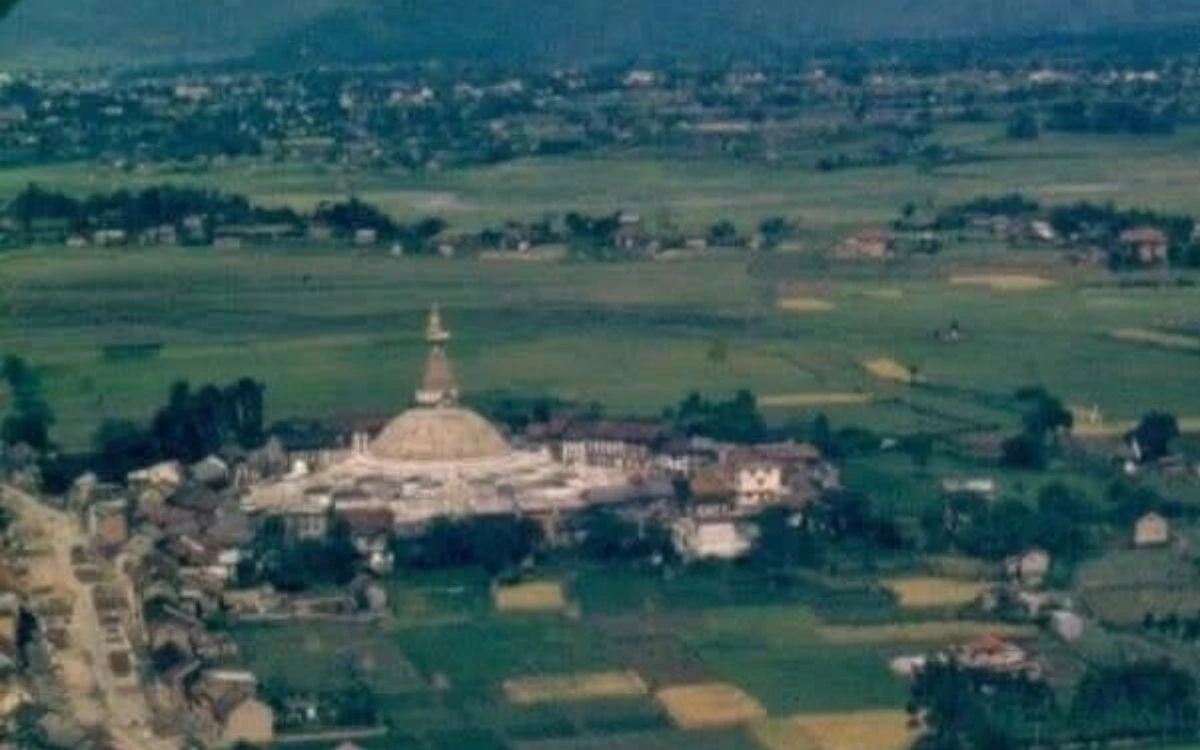 Aerial view of Boudhanath Stupa surrounded by green fields and traditional buildings in Kathmandu Valley