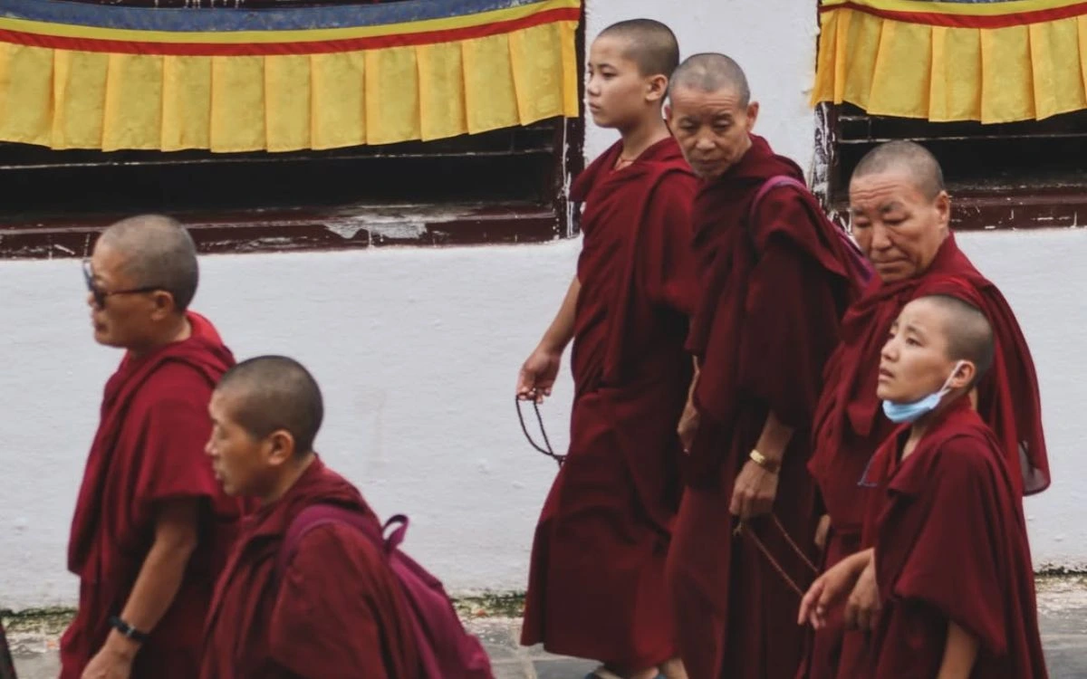 "Buddhist monks in traditional maroon robes walking at Boudhanath Stupa temple complex