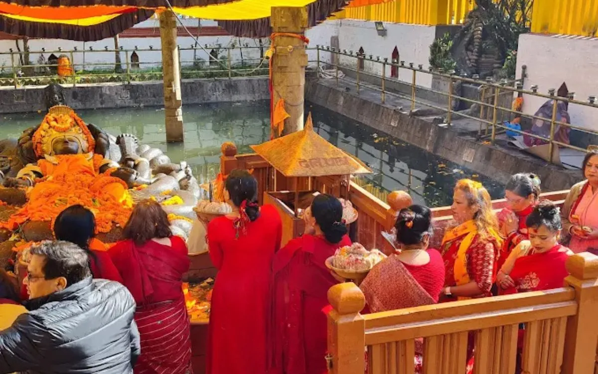 Hindu devotees in red sarees offering prayers to the reclining Vishnu statue at Budhanilkantha Temple pond, Kathmandu, Nepal