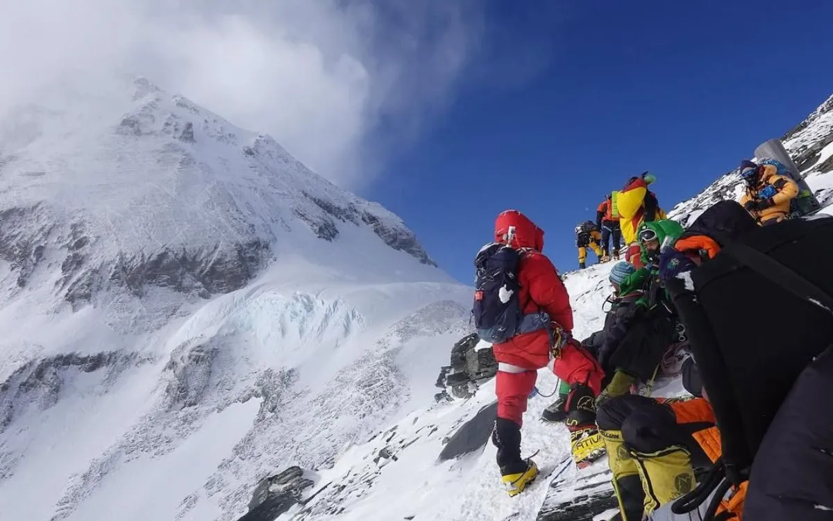 Climbers ascending Everest with colorful gear against rocky mountain face
