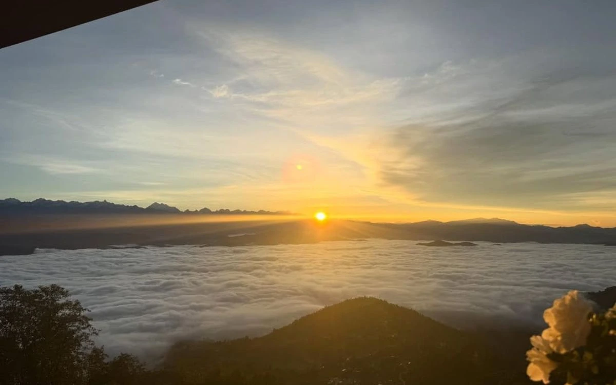 Golden sunrise over a layers of misty hills with the snow-covered Himalayan range in the distance.
