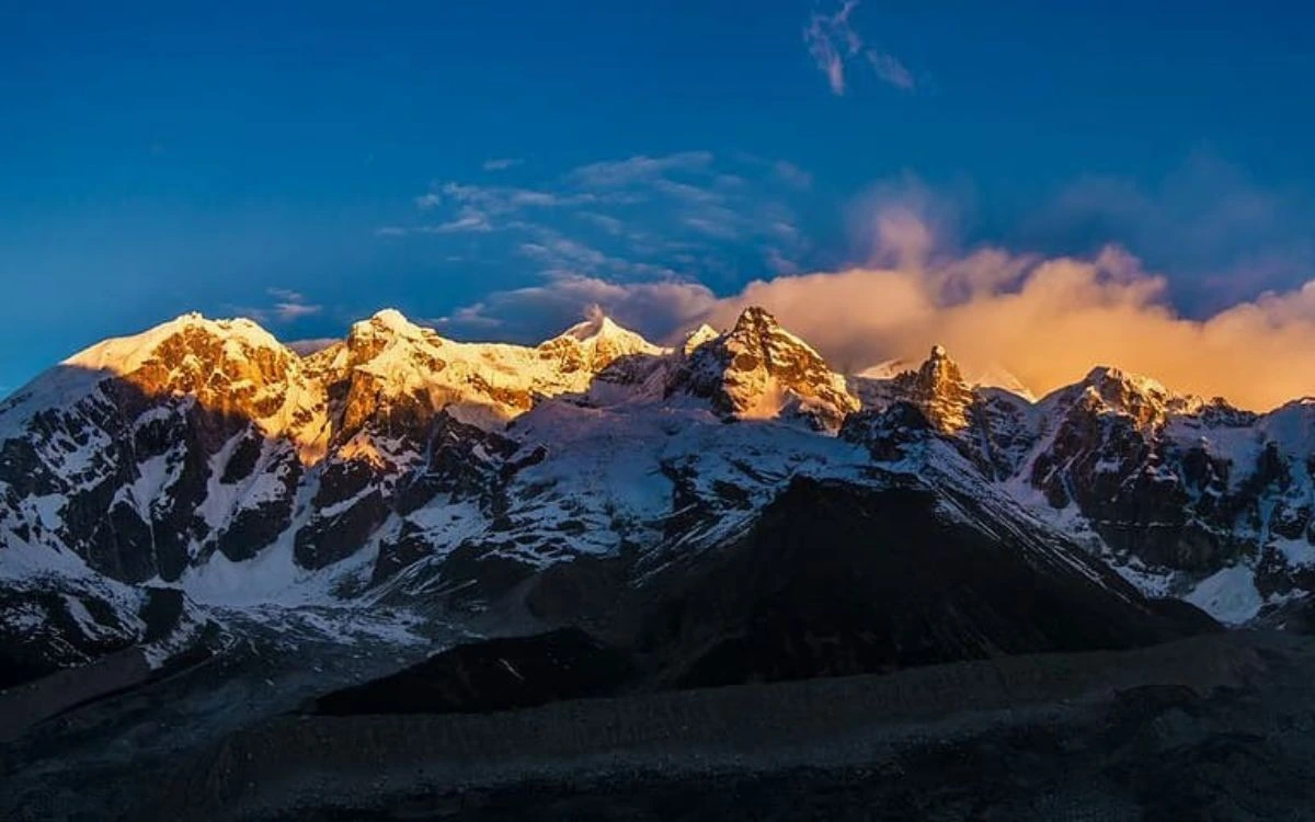 Golden alpenglow lighting the snow-covered Kanchenjunga massif at sunrise against a deep blue sky