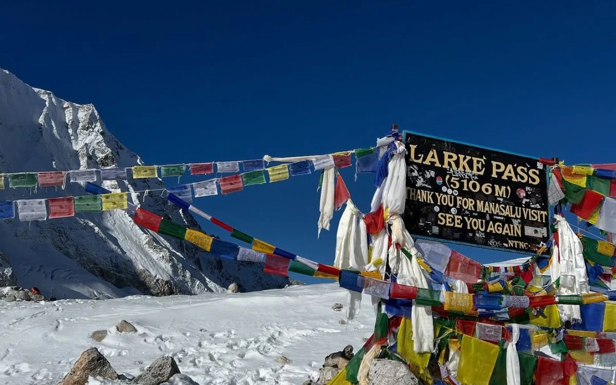 Larkya Pass sign at 5,106m decorated with colorful prayer flags