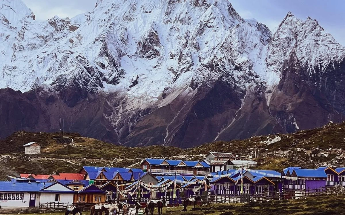 Traditional mountain village with blue-roofed buildings beneath towering Himalayan mountains