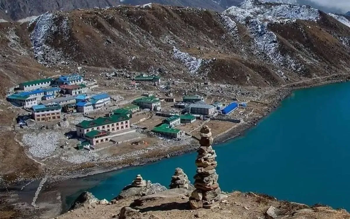 Mountain teahouse lodges beside turquoise glacial lake with stone cairns in foreground