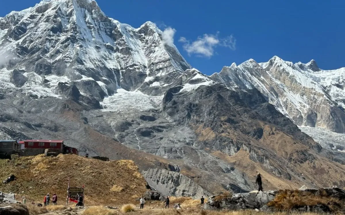Trekkers at base of massive snow-covered Himalayan mountain with glaciers