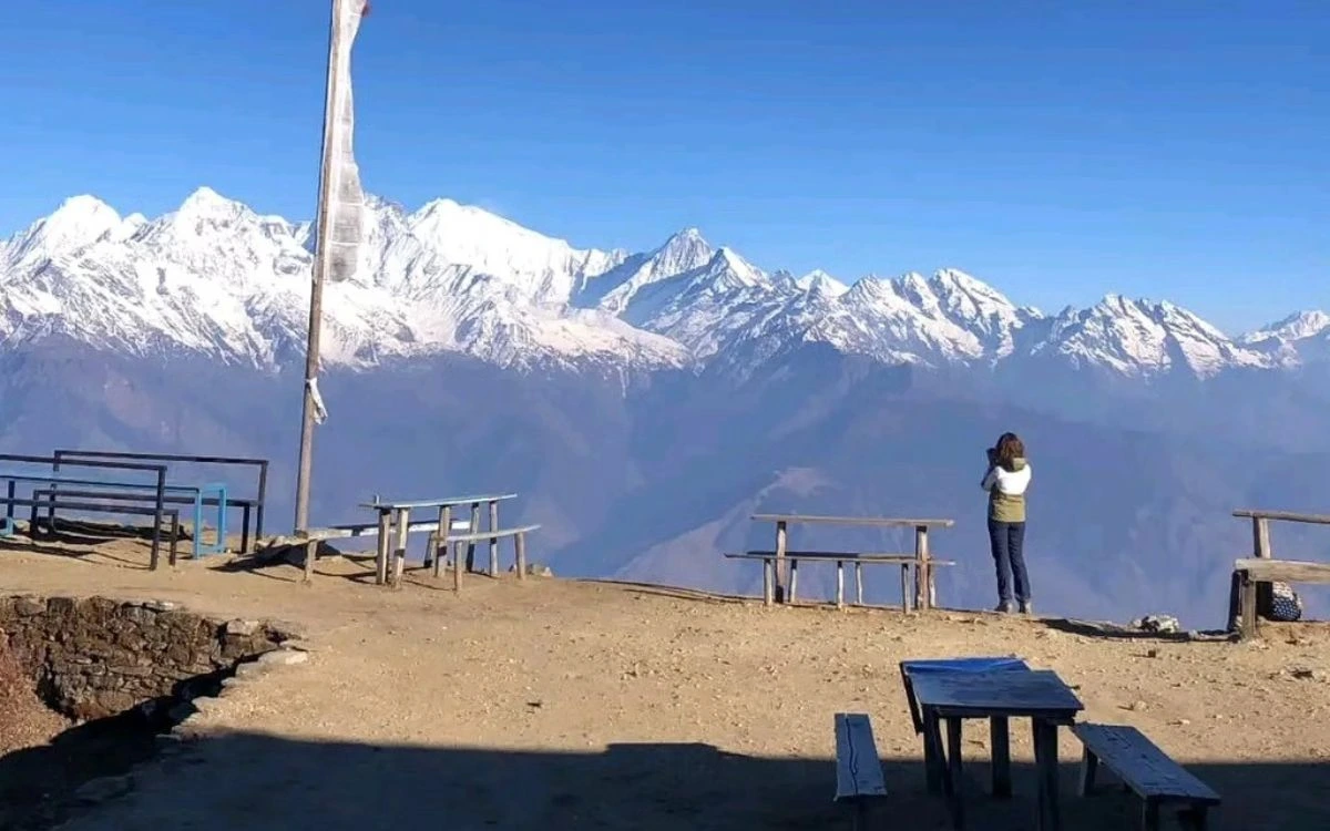 A trekker photographing a panoramic Himalayan mountain range from a high-altitude viewpoint