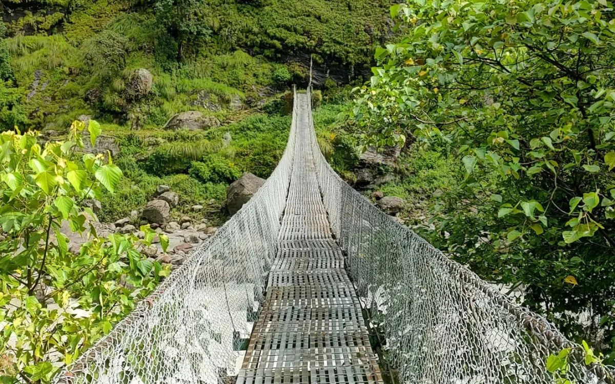 Suspension bridge with metal walkway crossing over a stream in Dharapani