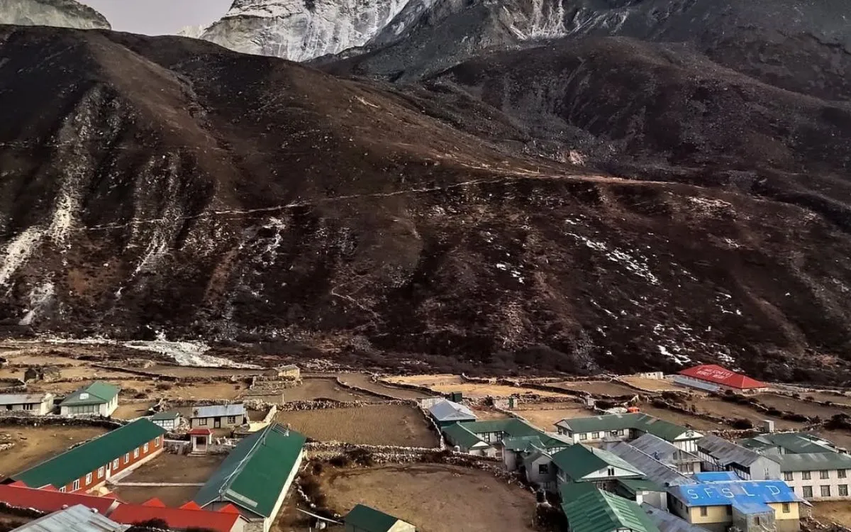 Dingboche settlement with green and blue-roofed teahouses in valley surrounded by autumn vegetation and mountains