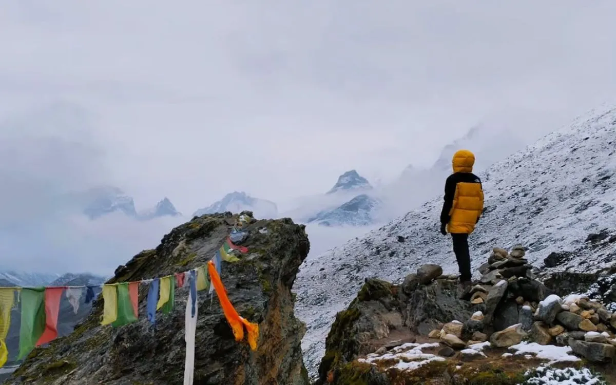 Hiker on Nangkartshang Peak with prayer flags and misty Himalayan views