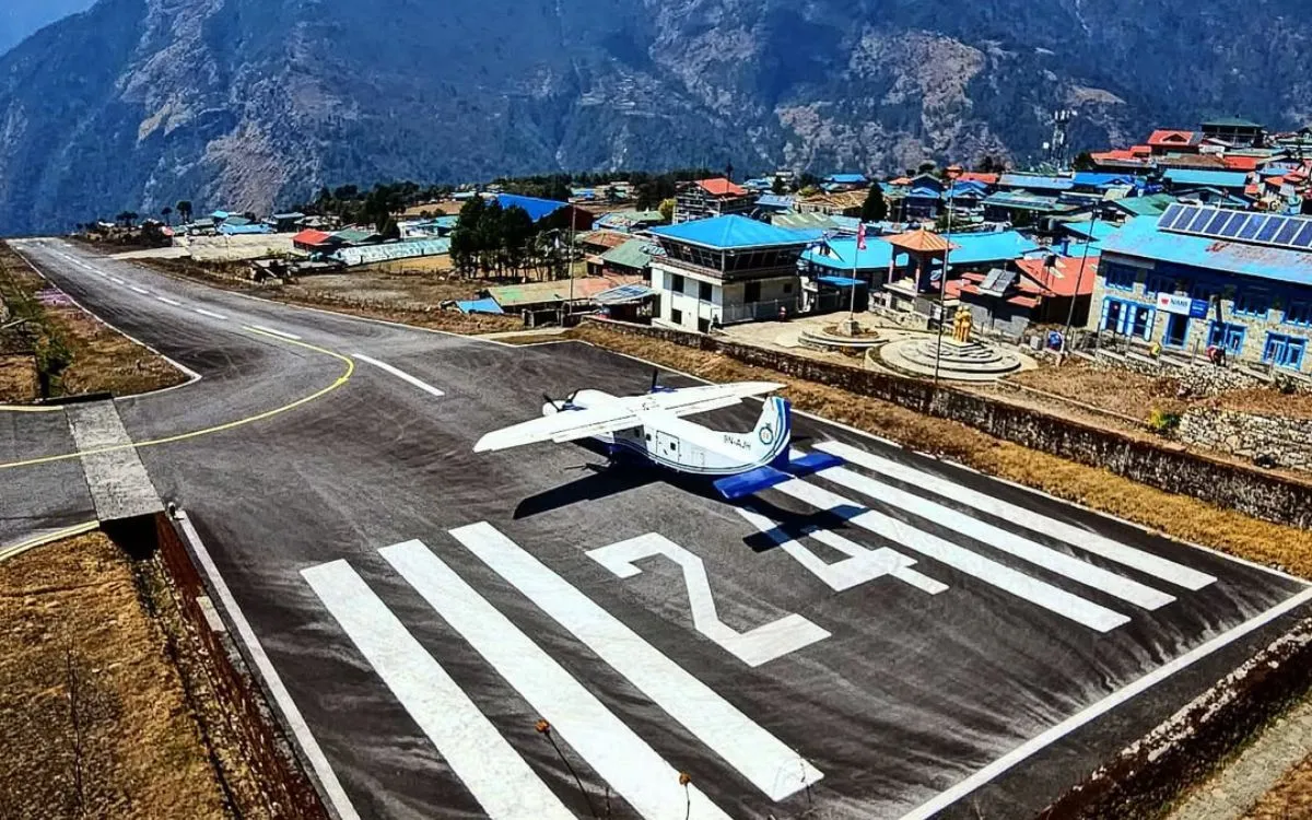  Lukla Airport runway with small aircraft and colorful mountain village buildings in background