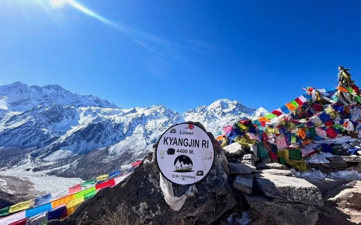 Mountain viewpoint at 4400m elevation marked with signage and colorful prayer flags, snowy peaks visible