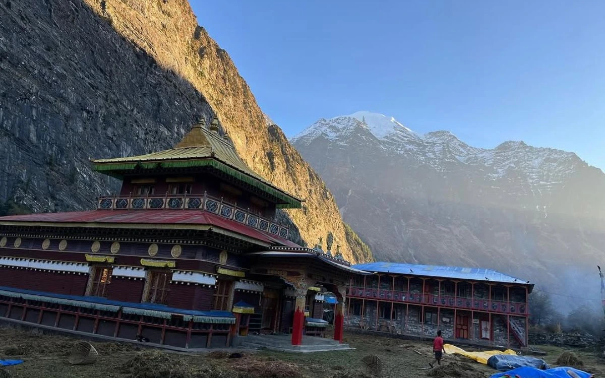 Traditional Tibetan monastery with golden roof against dramatic cliff and Mount Manaslu backdrop