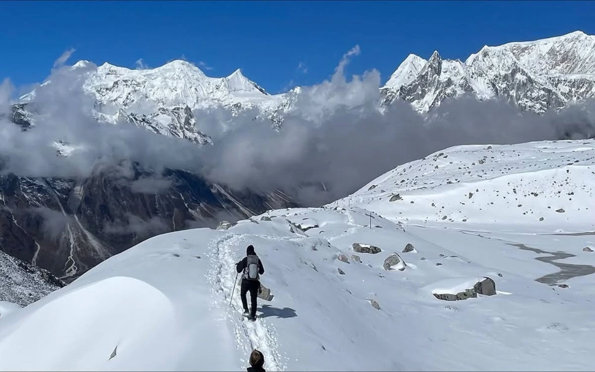 Trekker ascending snowy trail toward Manaslu peaks shrouded in clouds