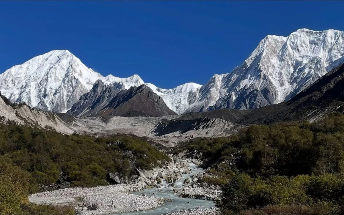 Glacial river flowing through green valley with Mount Manaslu massif towering above