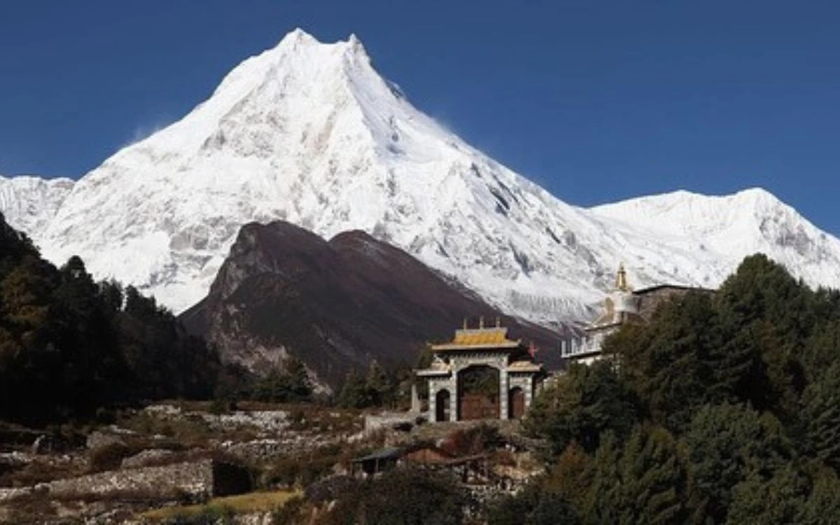 Mount Manaslu summit rising above Buddhist monastery gateway and forested hillside