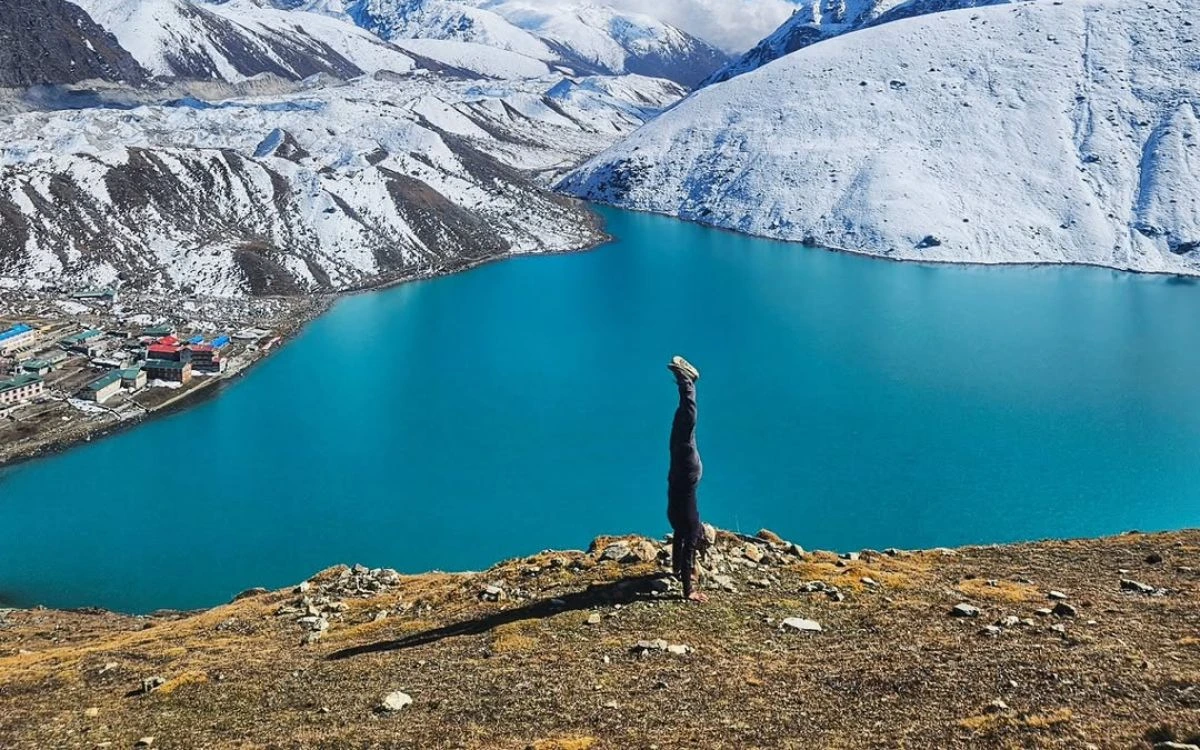 A trekker doing a handstand on a ridge overlooking the vivid turquoise Gokyo Lake and Gokyo village