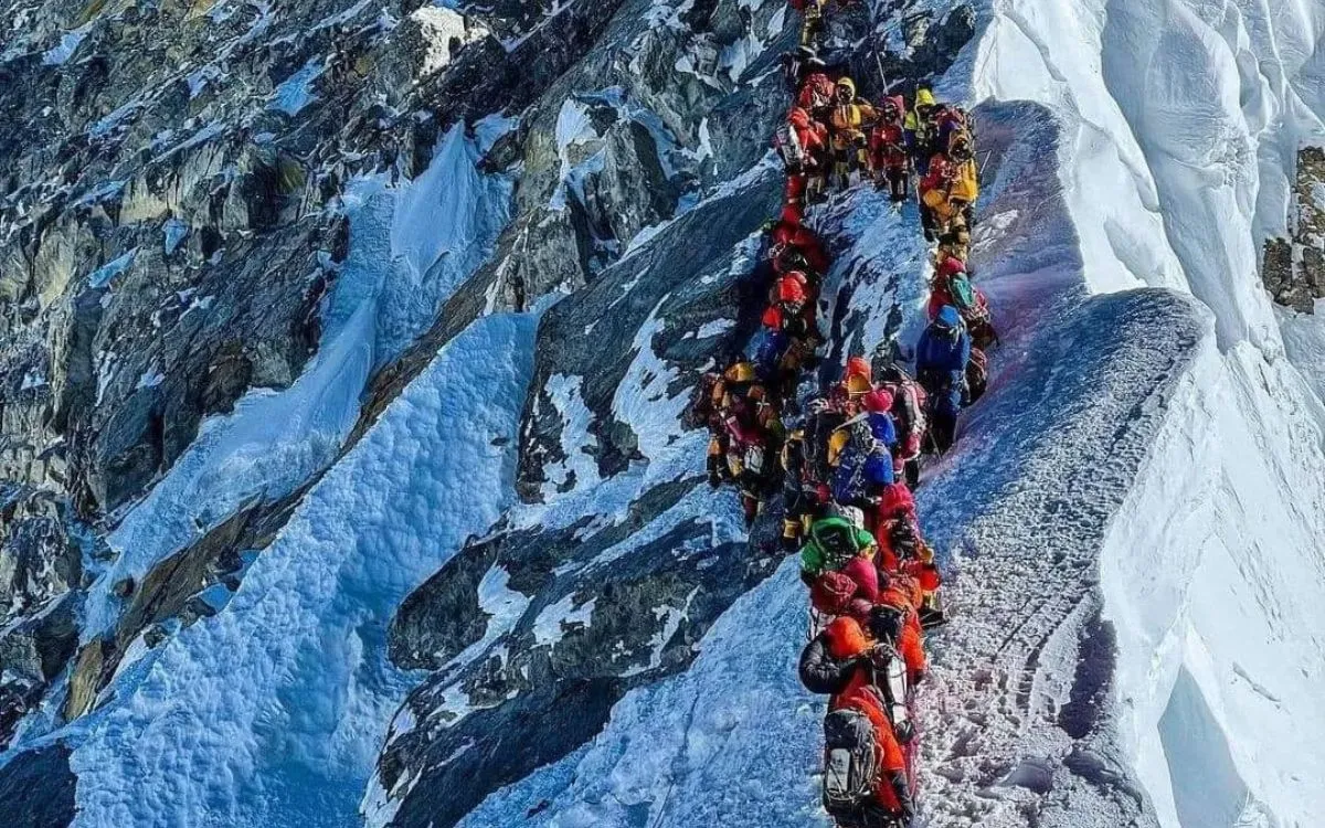 Mount Everest summit ridge with long queue of climbers in colorful mountaineering gear approaching the peak