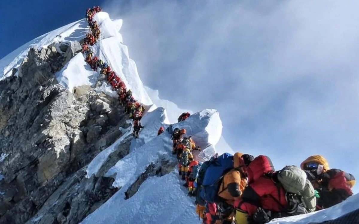 Dozens of climbers in colorful gear waiting in dangerous Everest traffic jam queue near summit