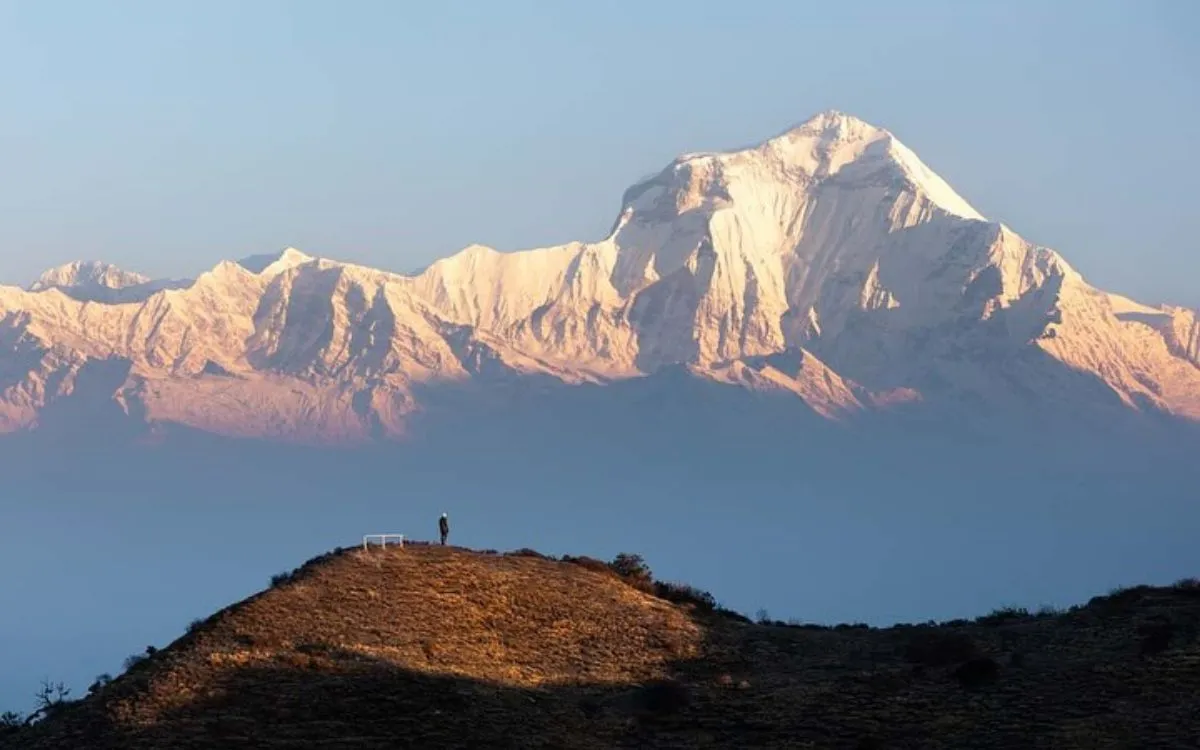 Solo trekker silhouette on hilltop viewing Dhaulagiri mountain range at sunset Khopra Ridge trek
