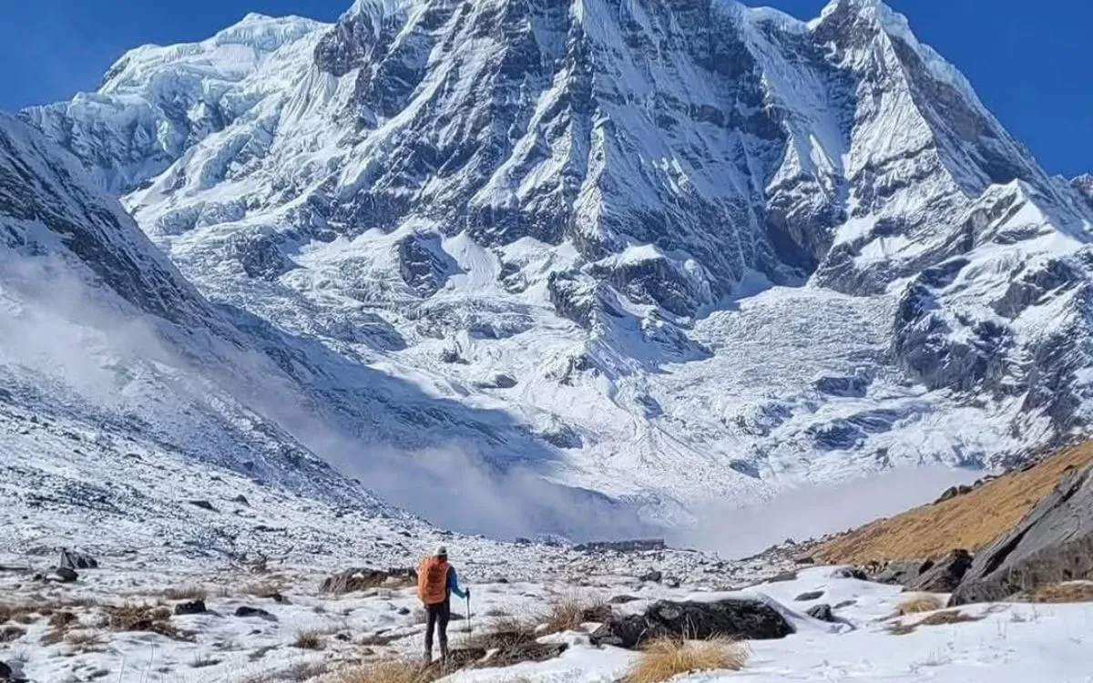 Trekker in orange jacket viewing massive glacier wall at Annapurna Base Camp Nepal