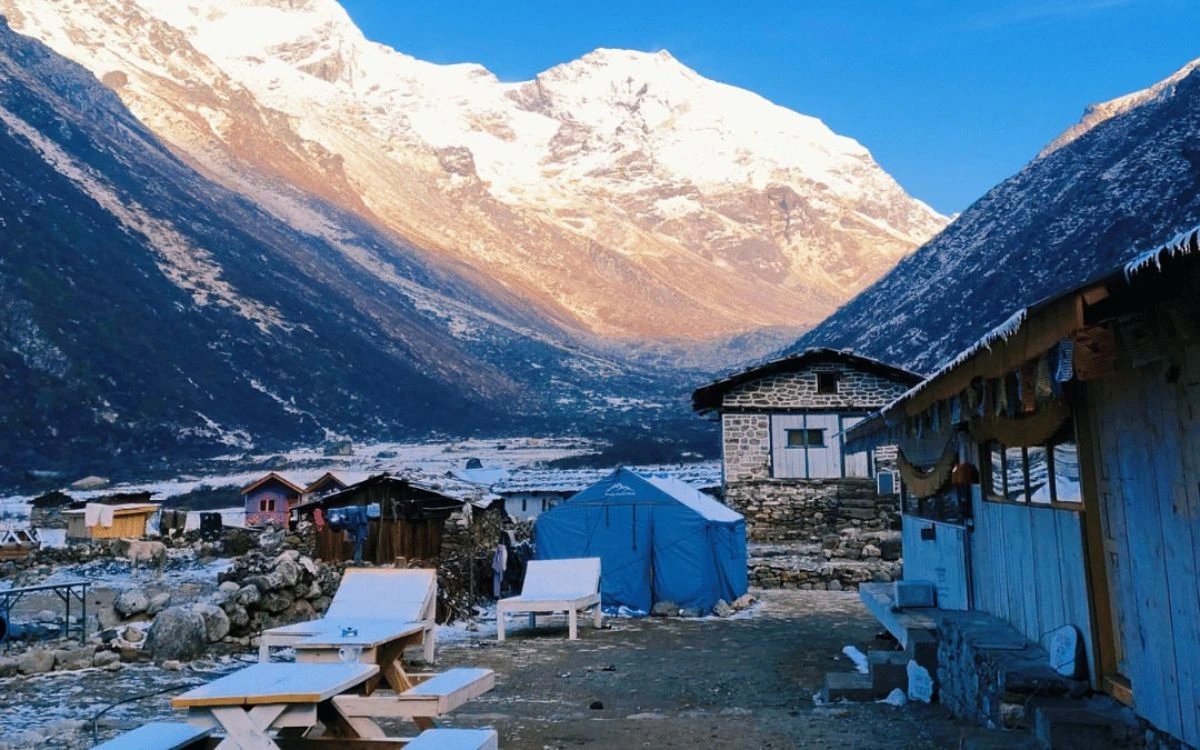 Stone teahouse and blue camping tent below snow-capped peaks on the Kanchenjunga trek