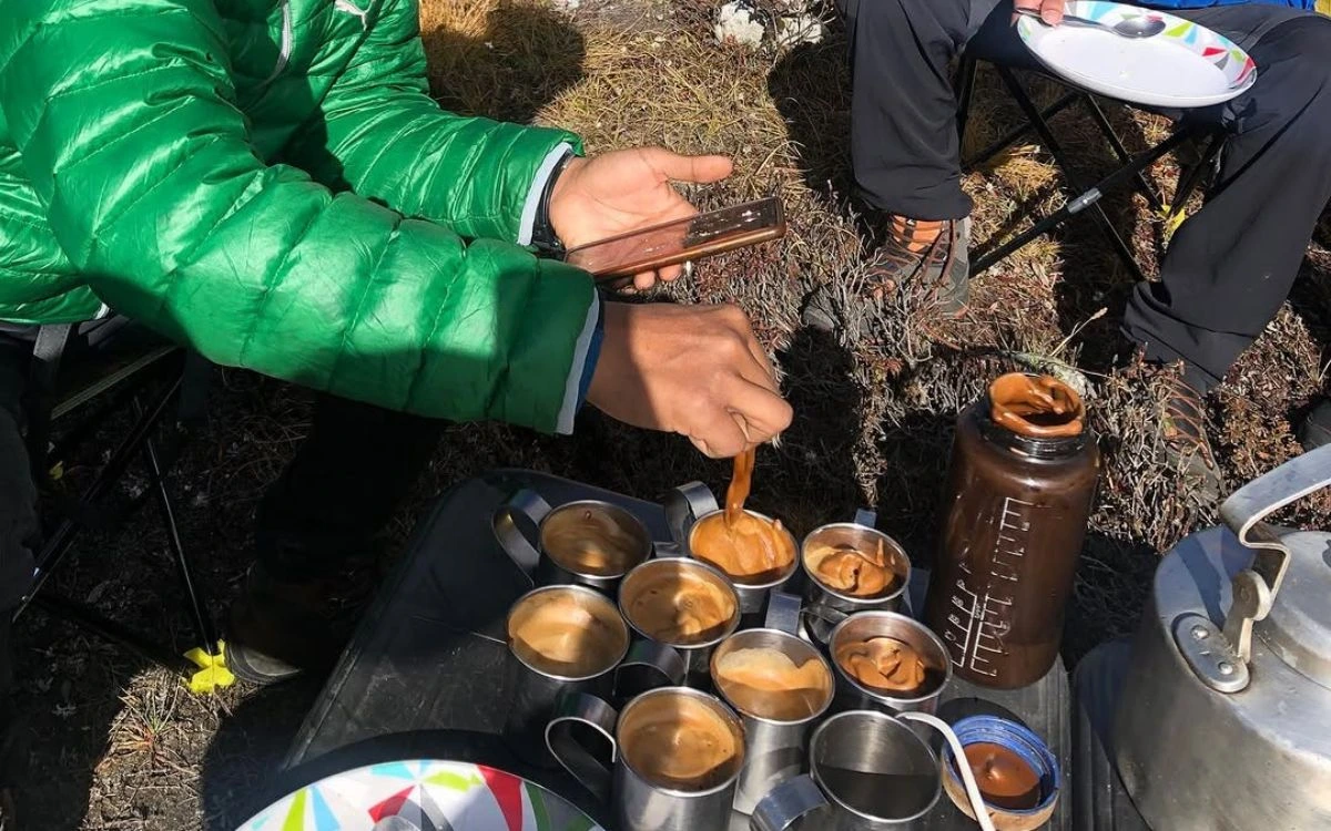 Trekkers pouring hot tea into cups, a typical mealtime scene on the Kanchenjunga trek