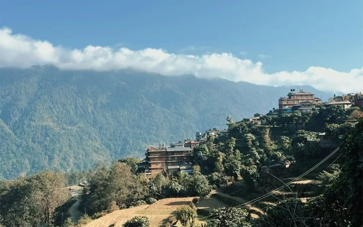 Multi-story traditional lodges and buildings on hillside in Ghandruk with forested mountains in background
