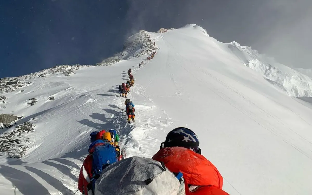 Line of climbers ascending snowy mountain ridge with summit peak visible in background