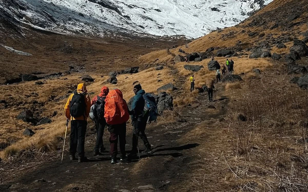 A group of trekkers in colorful jackets ascending a rocky trail toward a snow-covered slope in Nepal