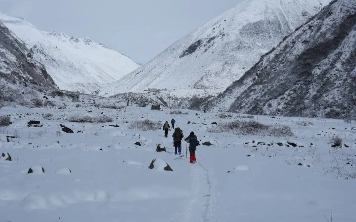 Trekkers walking through a snow-covered valley in Nepal with steep mountain slopes on either side