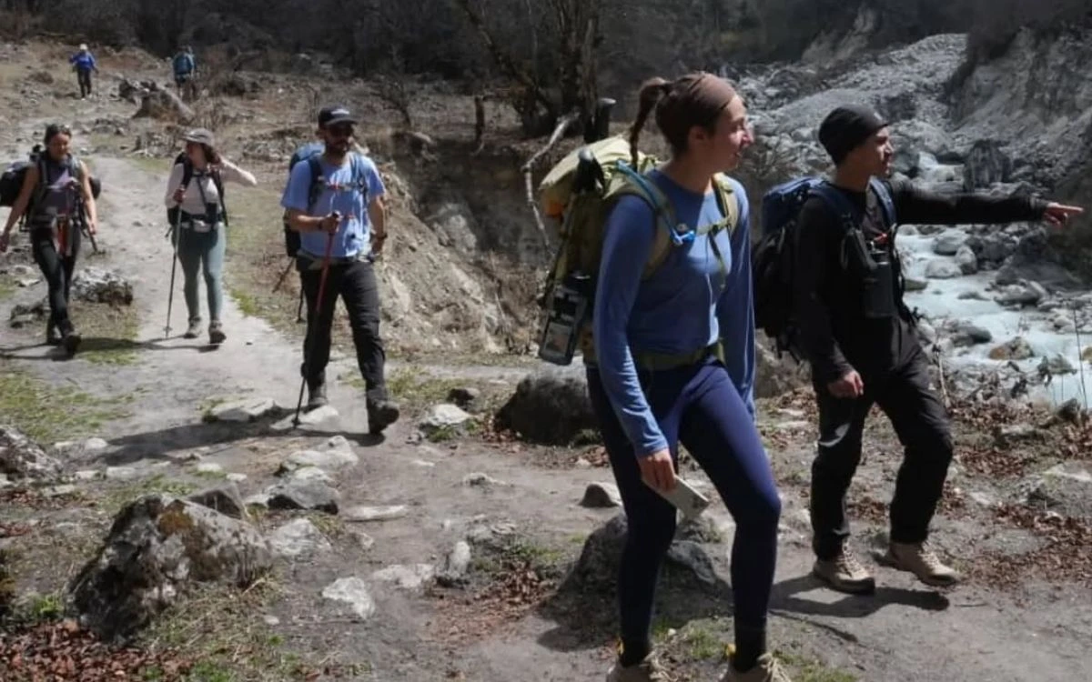 A group of trekkers with backpacks hiking along a rocky trail beside a glacial river in Nepal